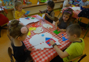 Czwórka dzieci wykleja kontur Polski wyciętymi elementami z papieru.